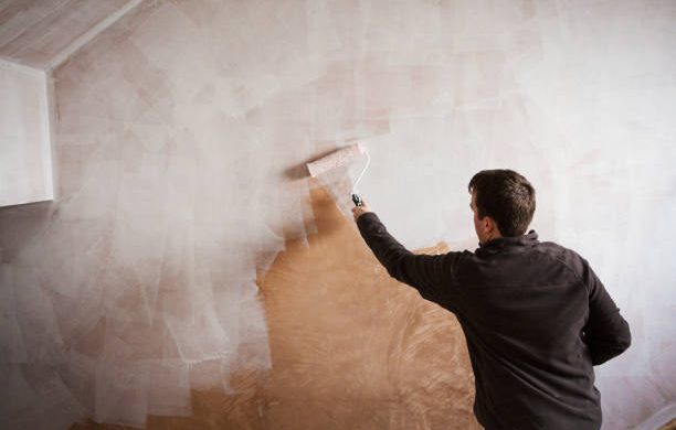 Homme qui peint un mur avec un rouleau et de la peinture blanche